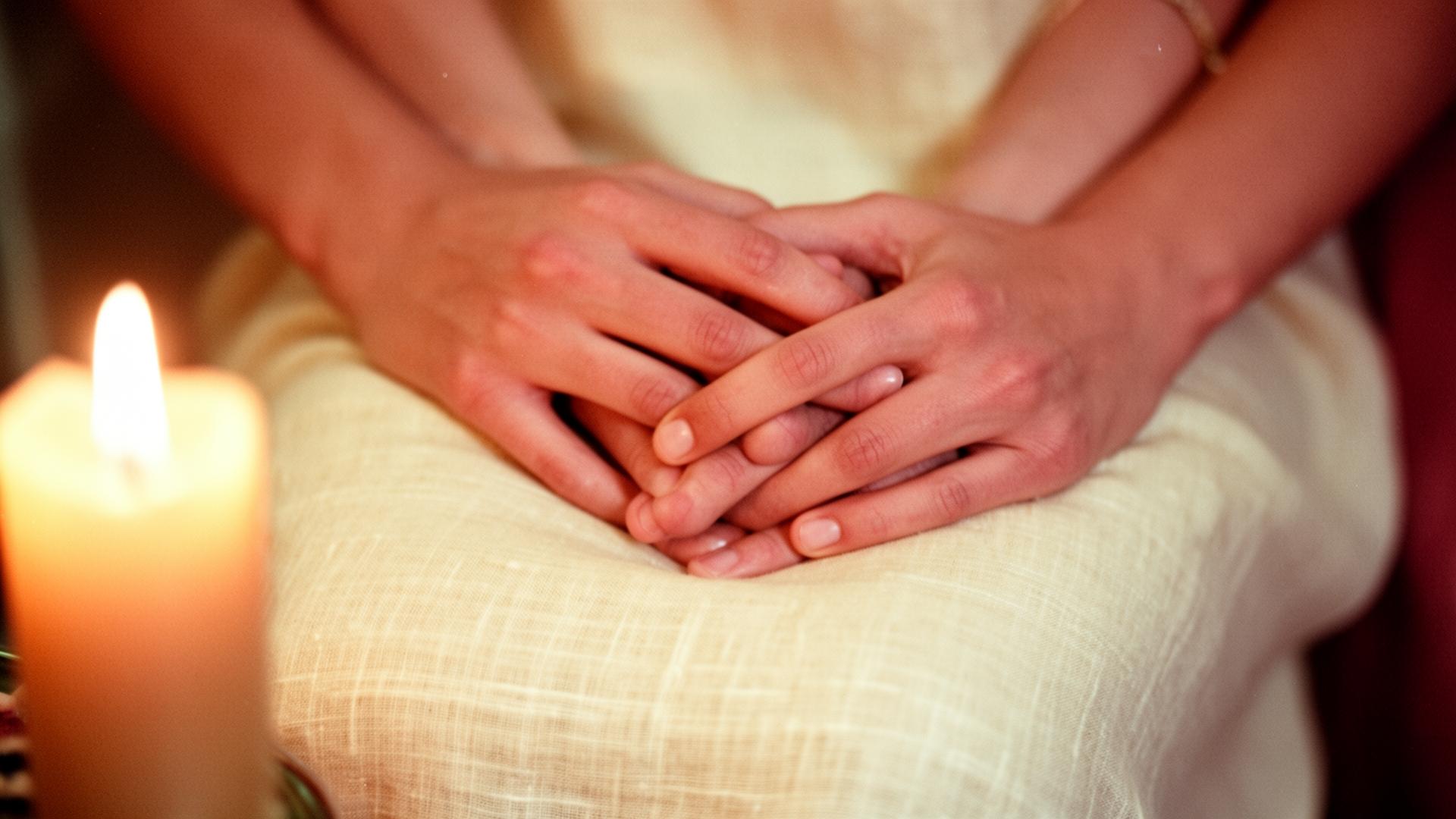 Two hands intertwined by candlelight on cream linen